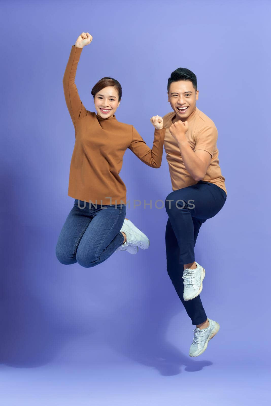 Photo of happy excited young loving couple jumping isolated over purple background.