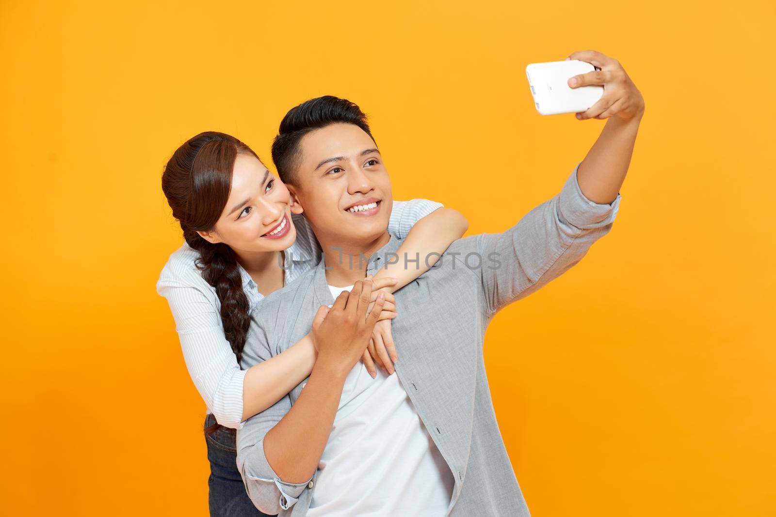 Young and beautiful couple expressing joy on camera while partying and taking selfie isolated over yellow background.