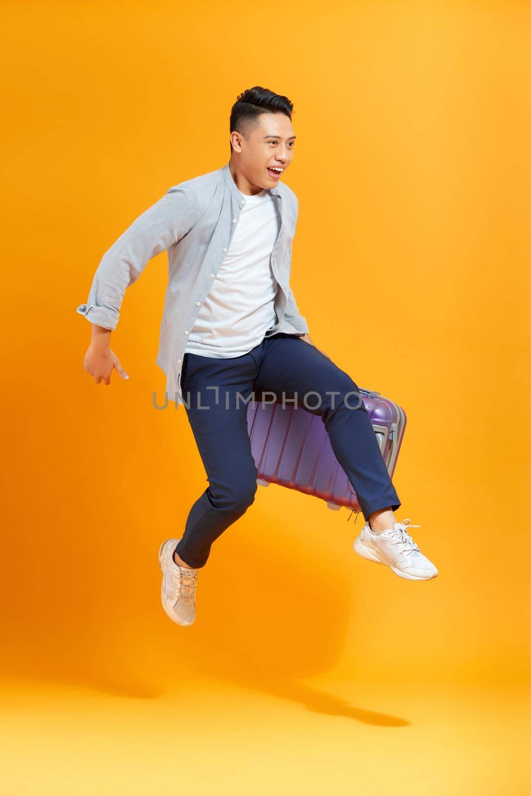 Young creative man is posing with suitcase on yellow background.