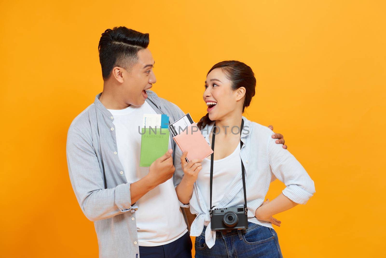 Successful lucky couple getting visa abroad holding raised fist showing passport with flying tickets shouting with wide open mouth 