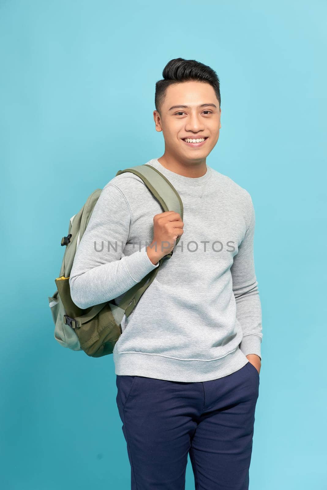 Handsome casual guy wearing backpack  laughing and looking away on blue.