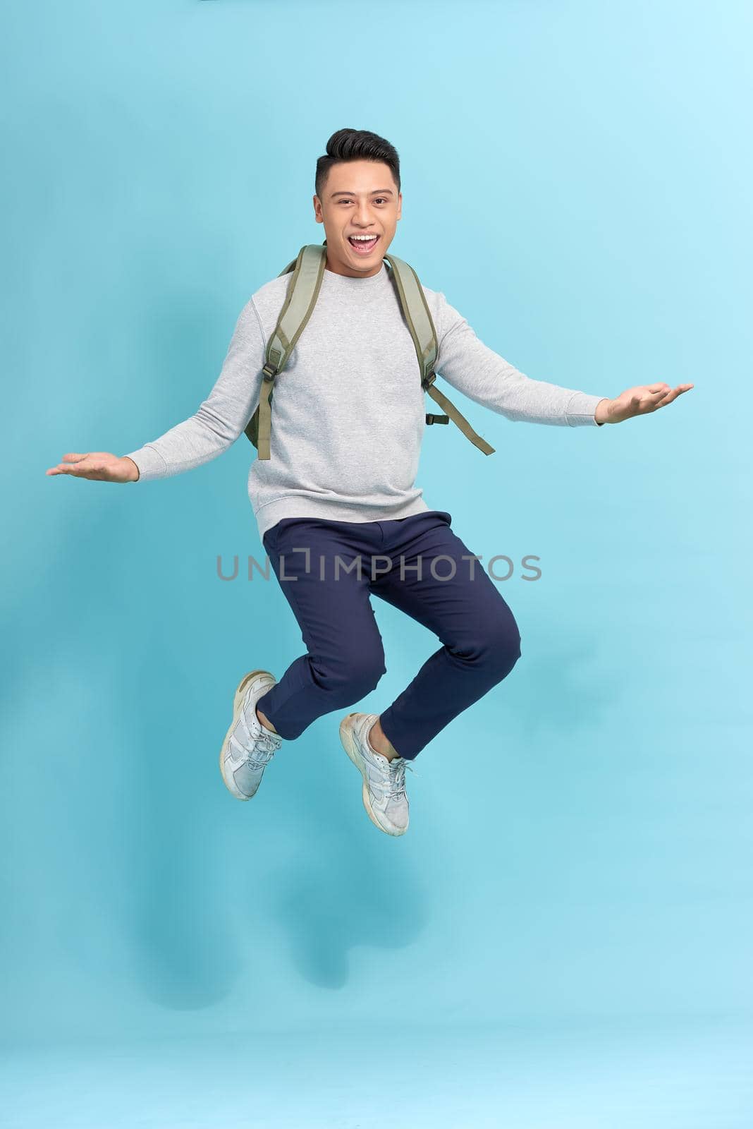 travel, tourism and people concept - happy smiling young man with backpack jumping in air over grey background