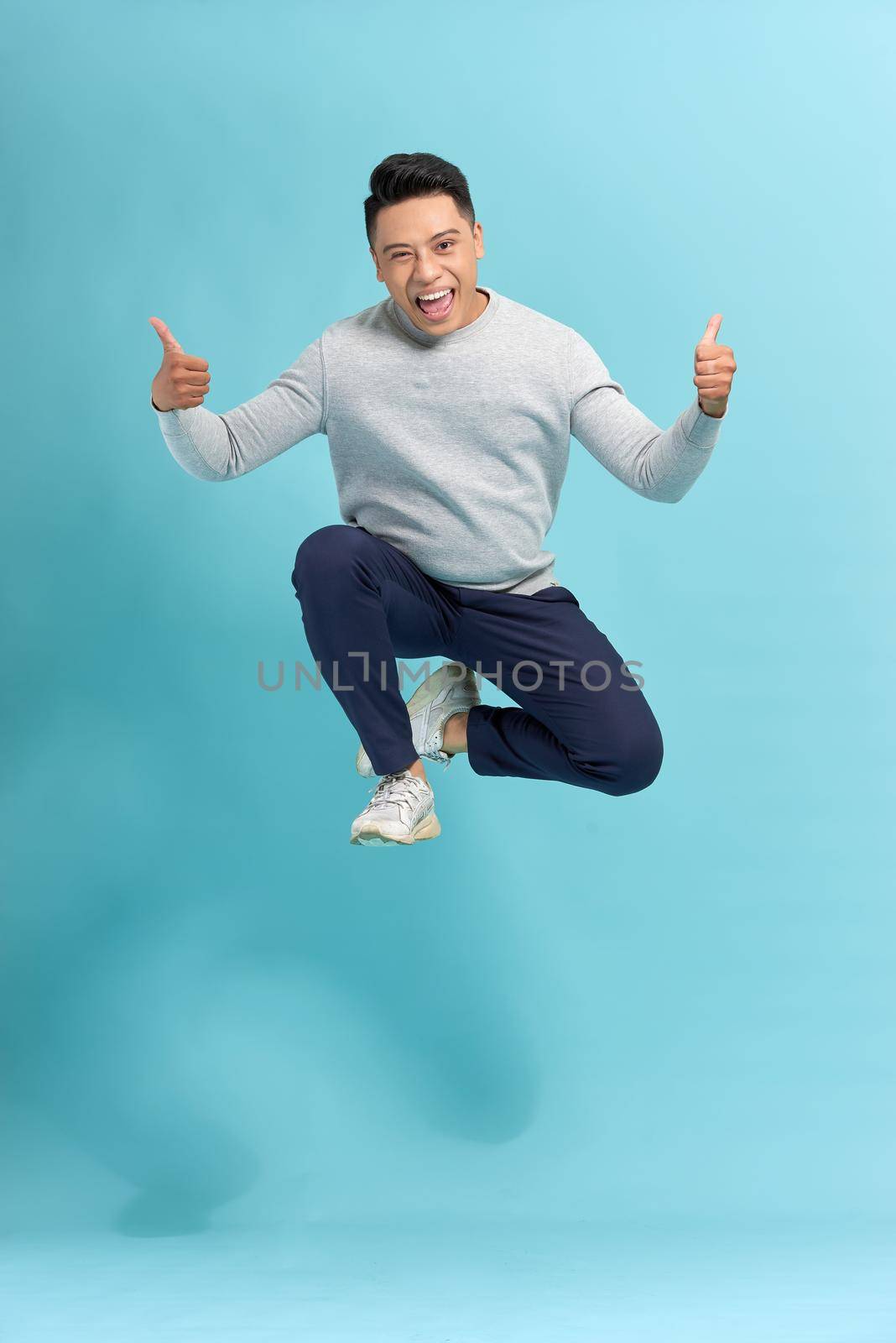 Full length portrait of a cheerful bearded man jumping and showing thumbs up