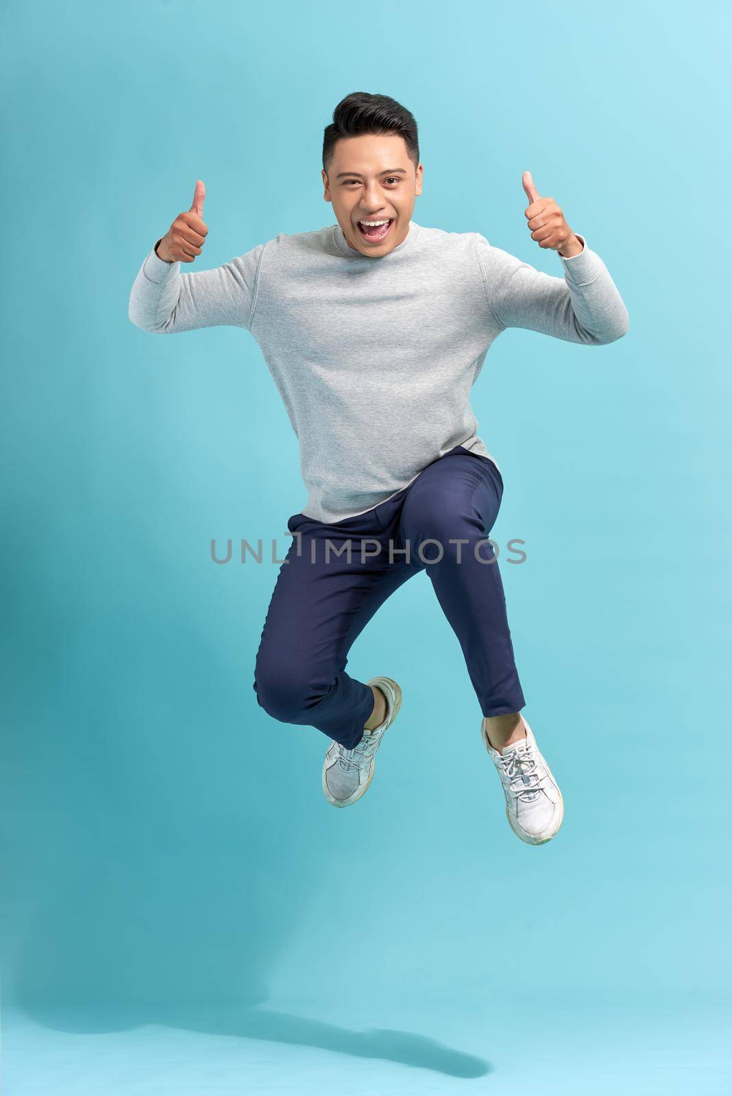Overjoyed guy jumping and showing thumbs up over blue studio background
