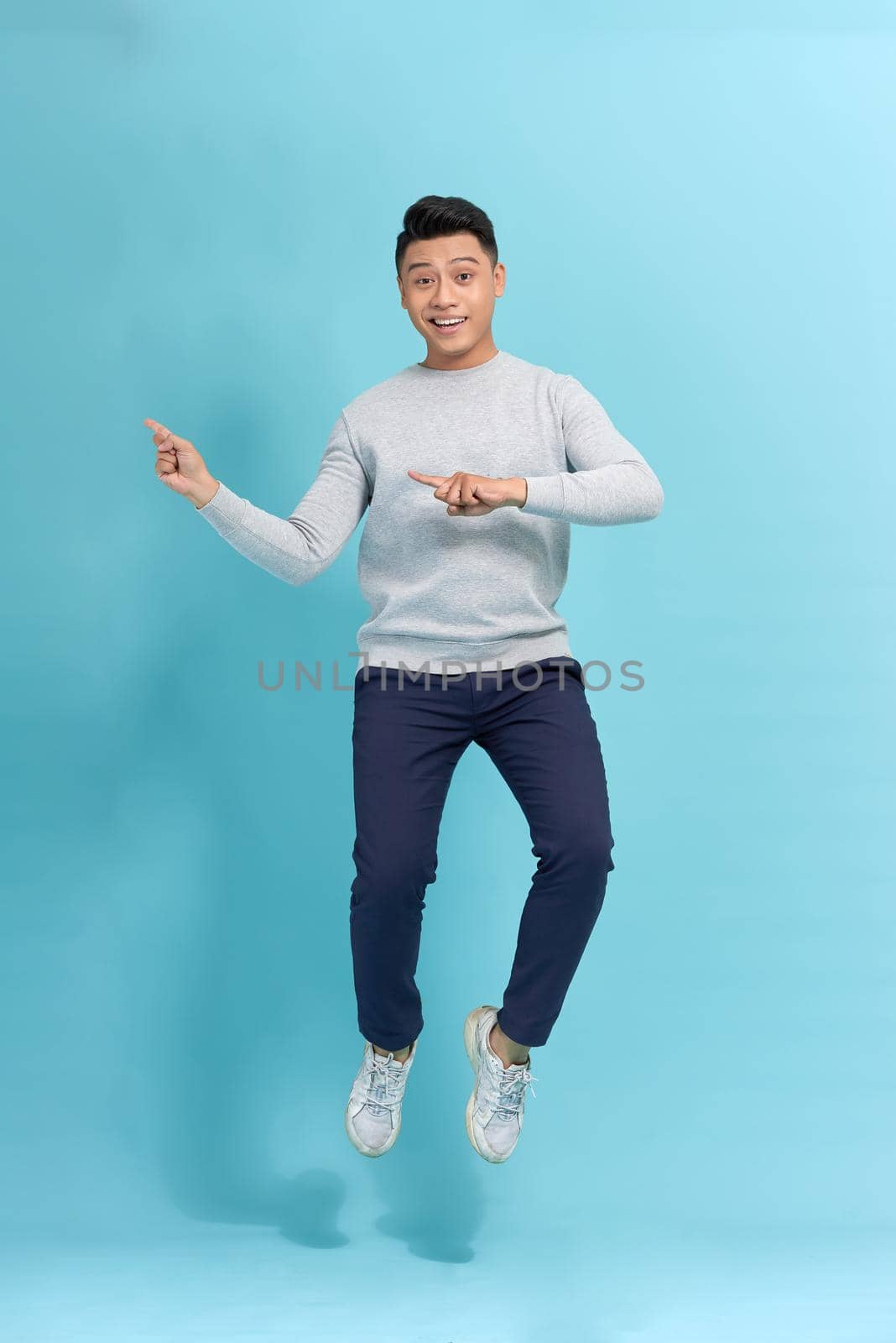 Happy, young, funny, attractive handsome man jumping in air and pointing index fingers to the side over blue background