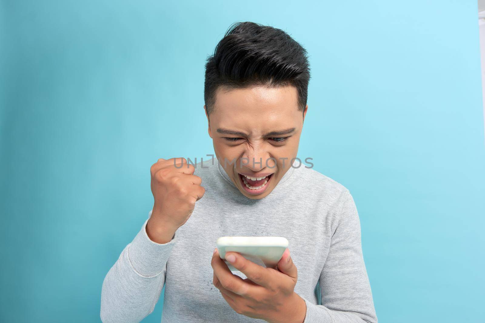 Angry man screaming on the phone isolated on a blue background