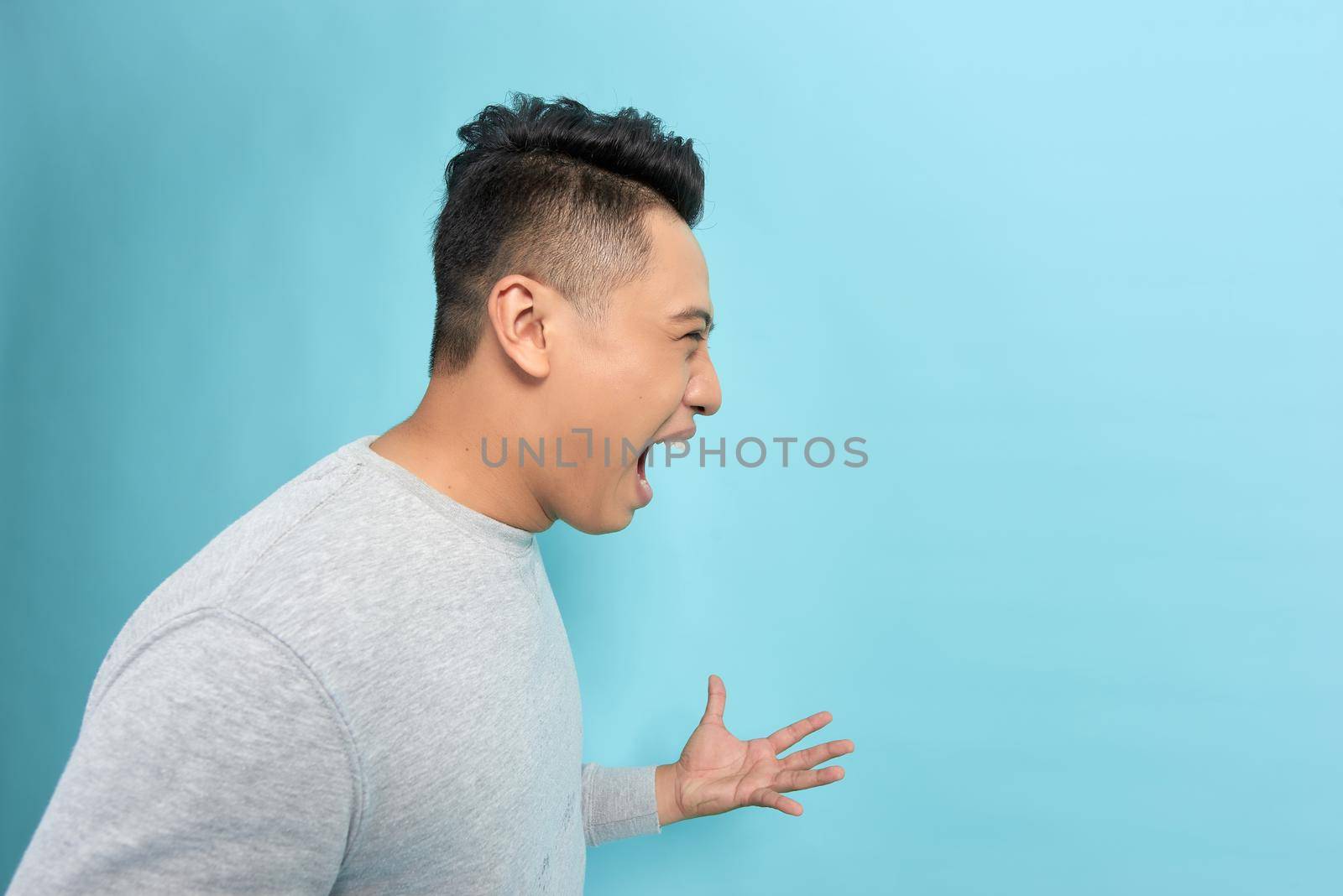 Closeup side view profile portrait of angry upset young man isolated on blue background.