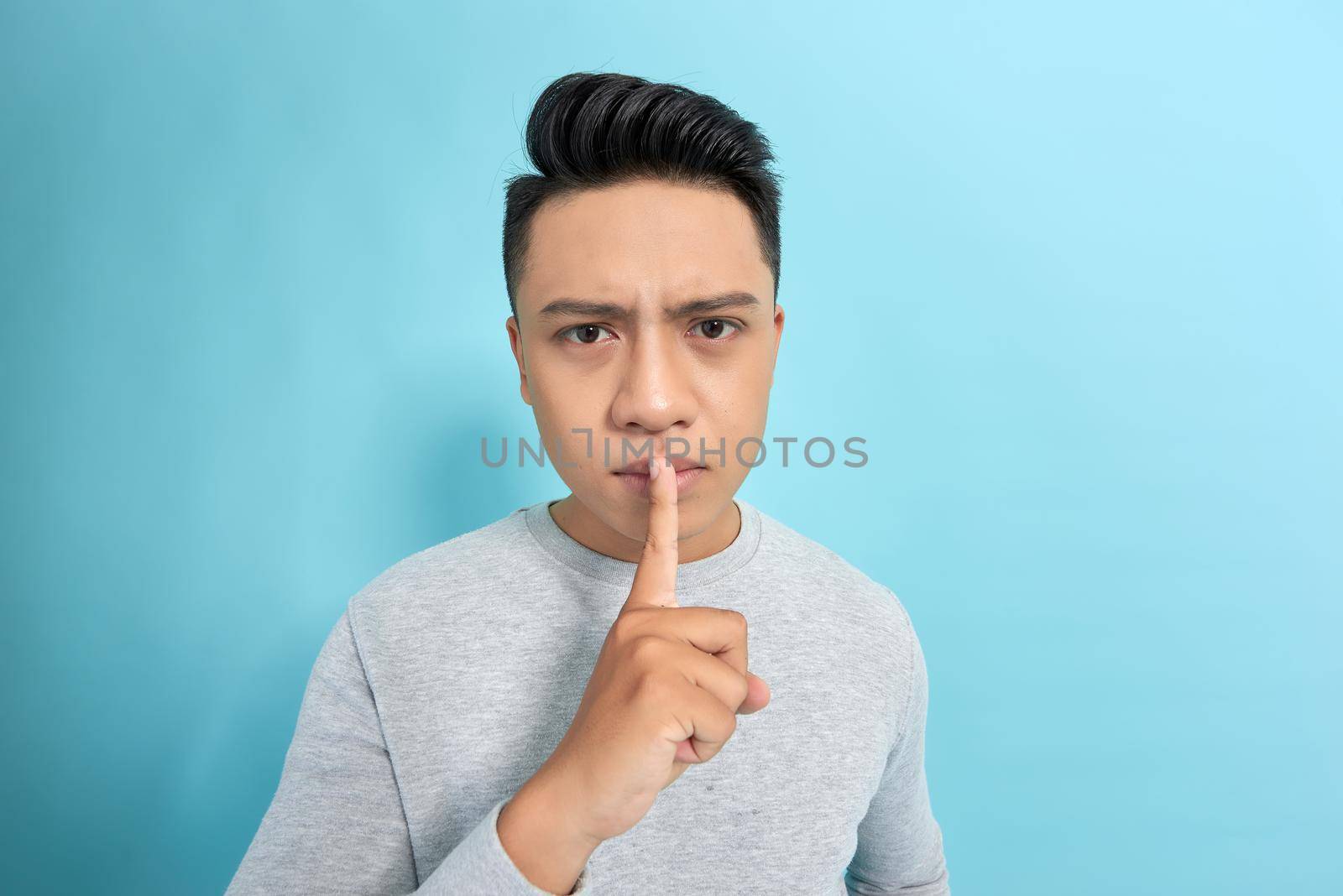 Young handsome man asking for silence and quiet, gesturing with finger in front of mouth, saying shh or keeping a secret