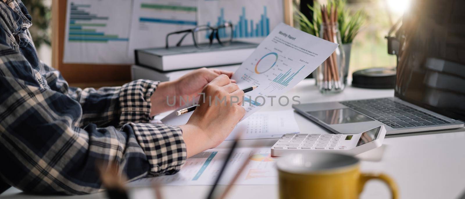 Close up of businessman or accountant hand holding pen working on calculator to calculate business data, accountancy document and laptop computer at office, business concept. by nateemee
