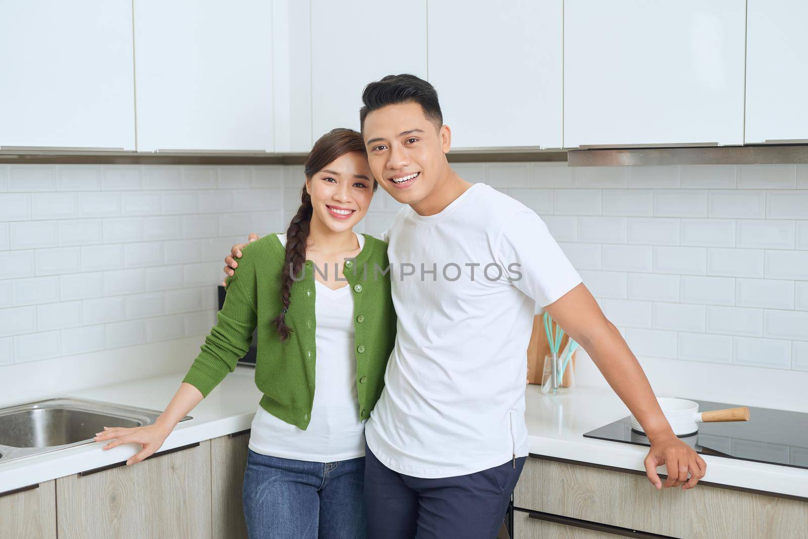 Attractive young woman and handsome man are enjoying spending time together while standing on light modern kitchen.