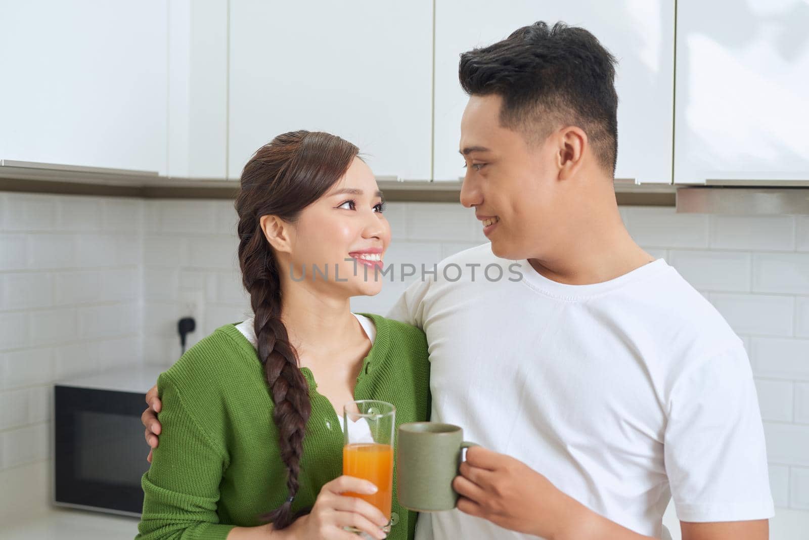 Attractive young woman and handsome man are enjoying spending time together while standing on light modern kitchen.