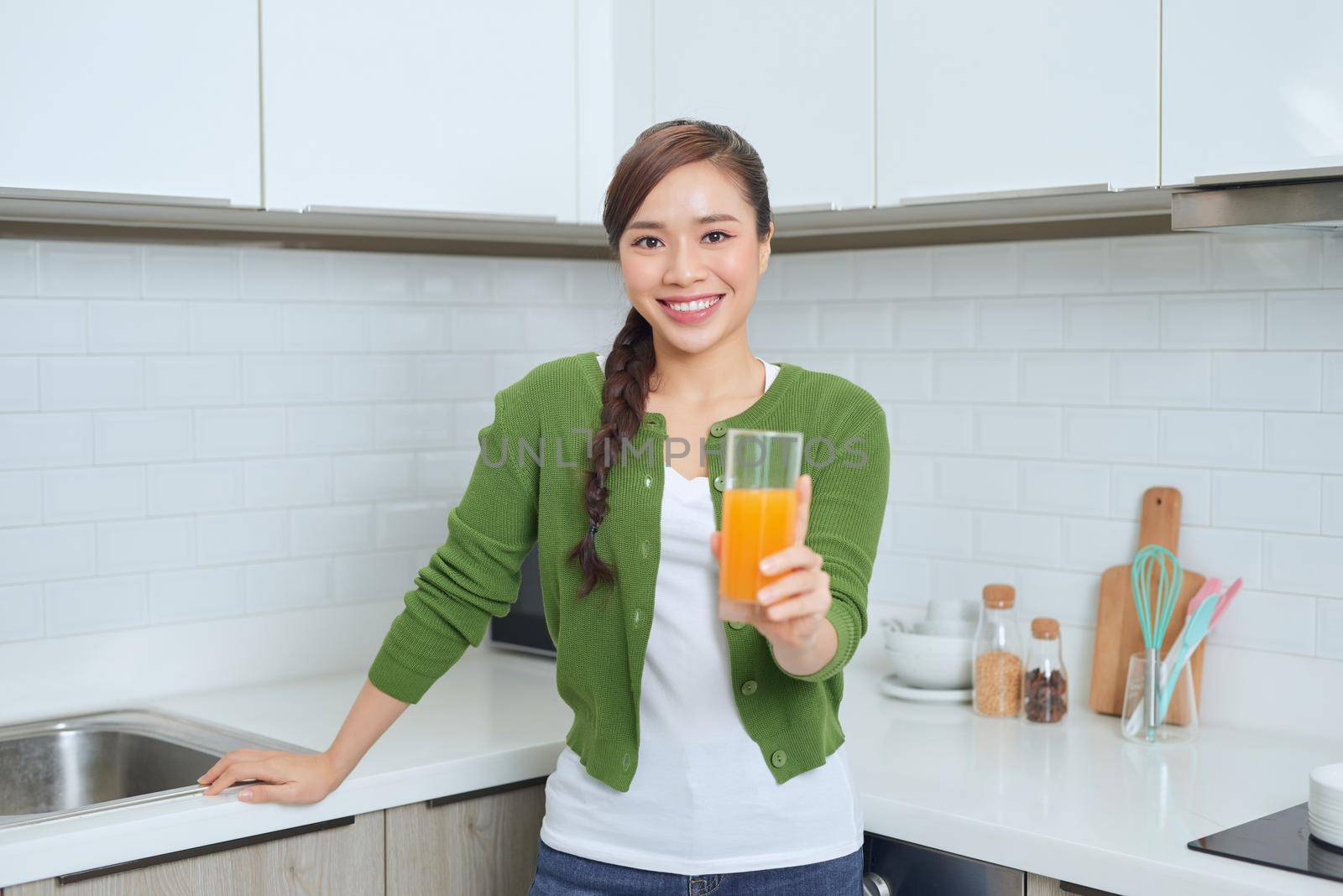 Portrait of a smiling young woman drinking orange juice in the kitchen at home by makidotvn