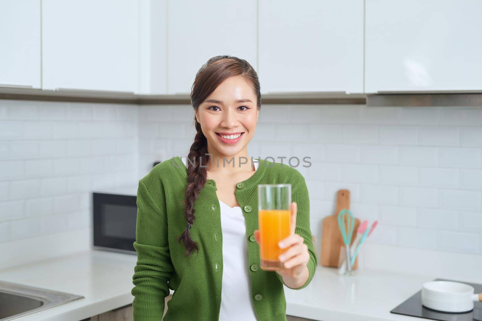 Portrait of a smiling young woman drinking orange juice in the kitchen at home