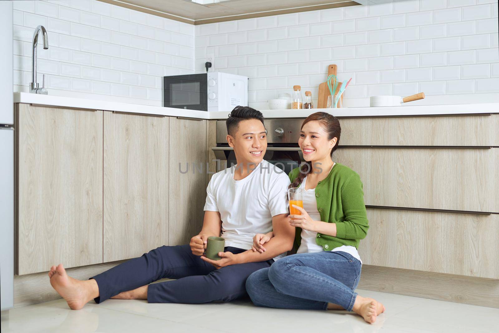 Love is in the air. Beautiful young couple drinking coffee and orange juice while sitting on the kitchen floor at home by makidotvn