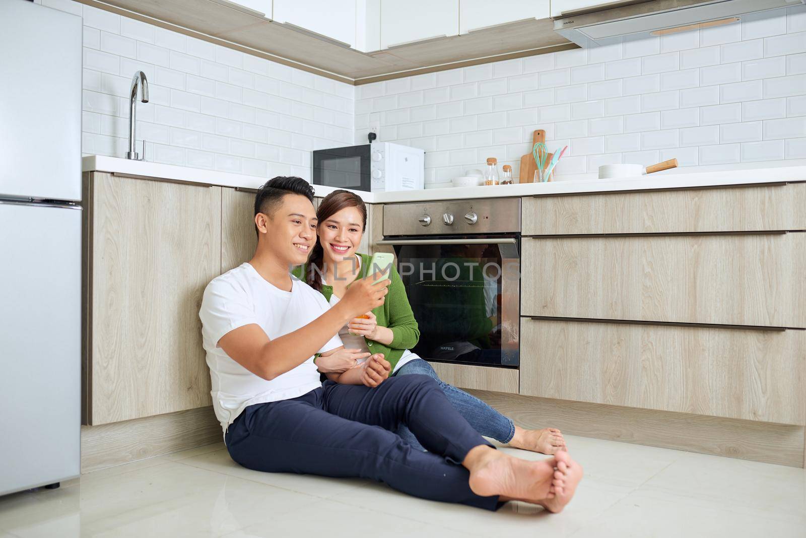Love is in the air. Beautiful young couple drinking coffee and orange juice while sitting on the kitchen floor at home