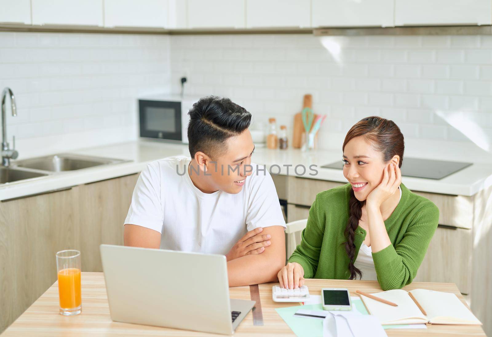 Photo of cheerful loving young couple using laptop and analyzing their finances with documents. Look at papers.