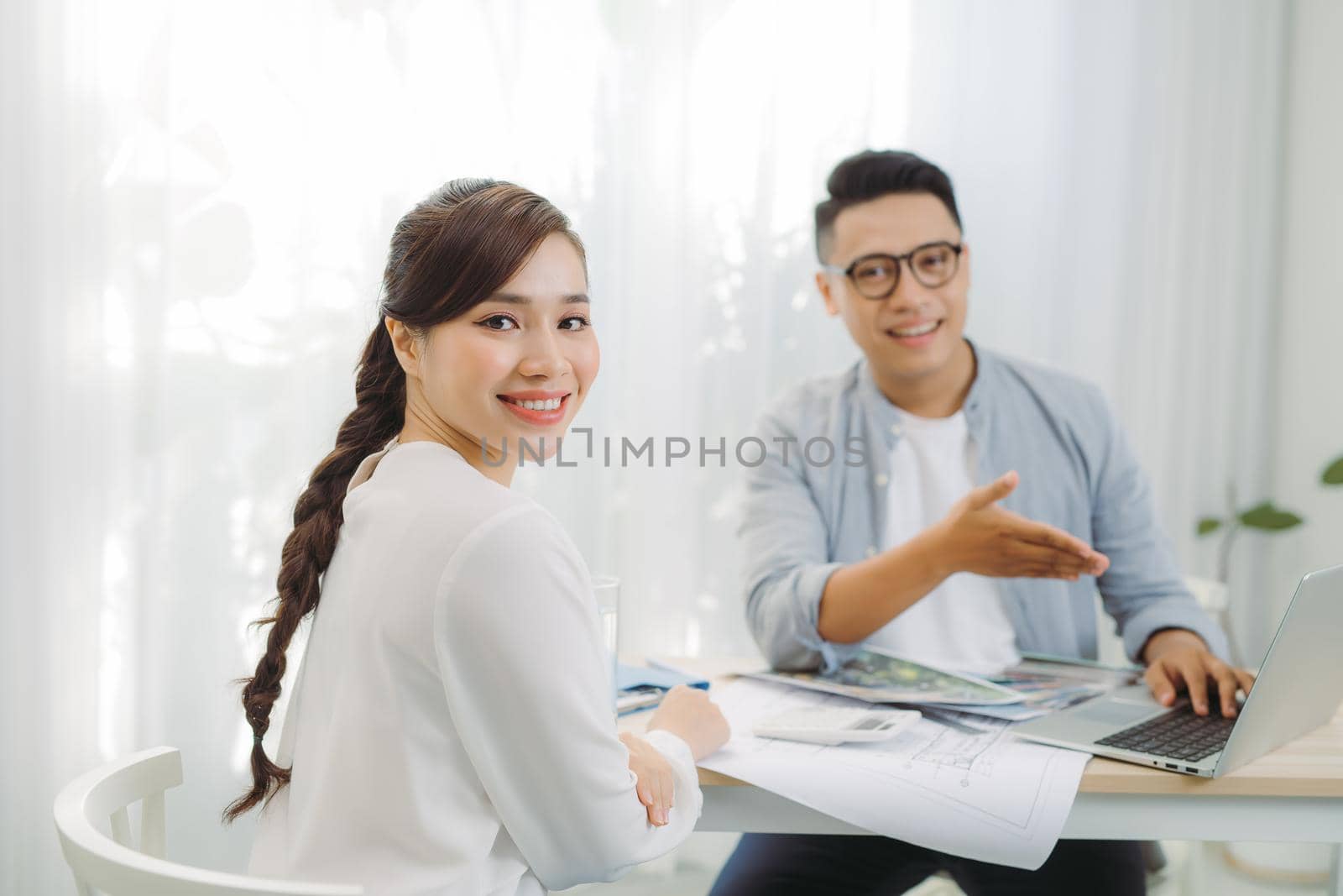 Male and female architect discussing a set of blueprints spread out on a table at office.