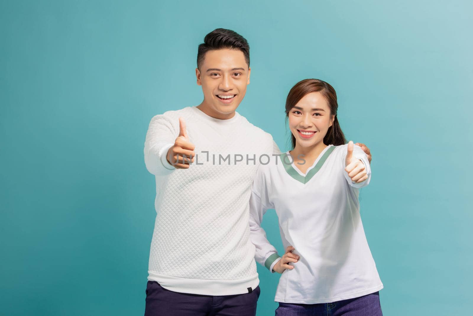 Happy young couple showing thumbs up and looking at camera isolated over blue background