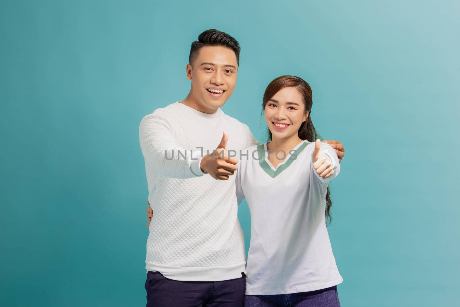 Happy young lovely couple showing thumbs up and looking at the camera over light blue background