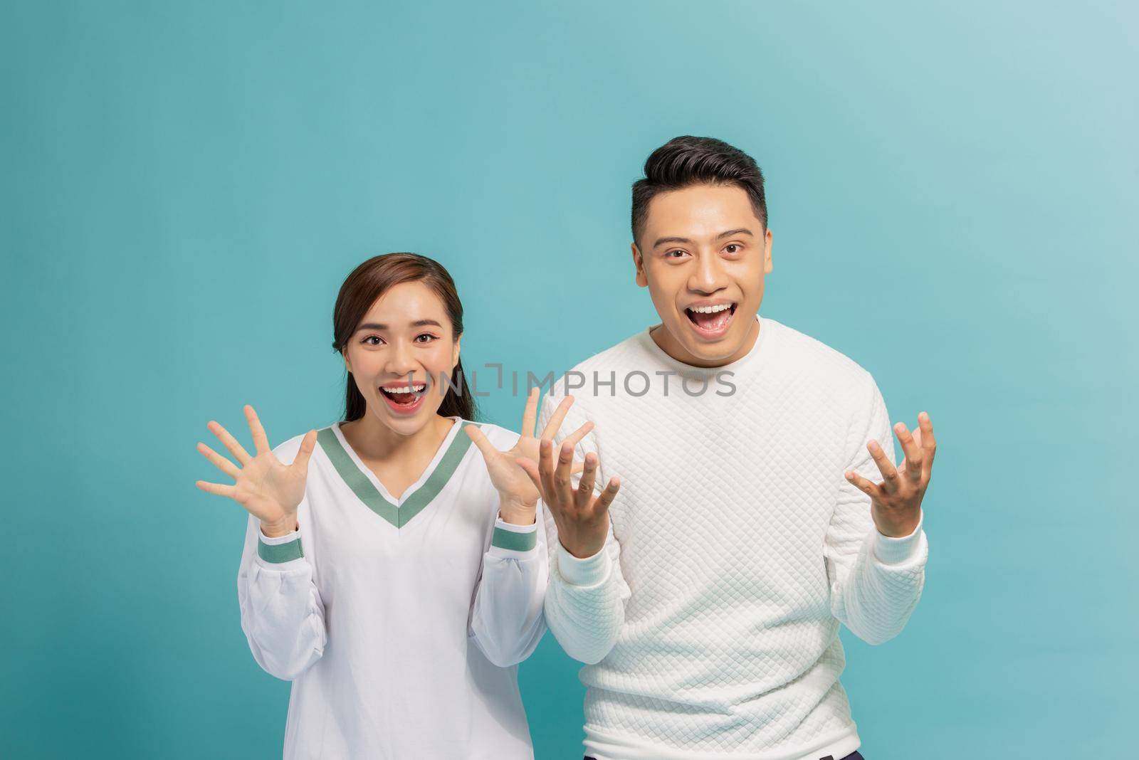 Portrait of optimistic amazed young couple man and woman with arms raised isolated over blue background by makidotvn