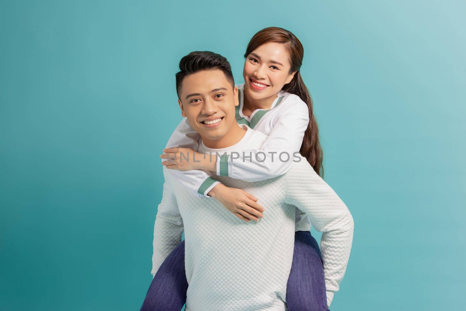 Piggyback ride. Young man carrying girlfriend on his back, blue background with copy space. by makidotvn