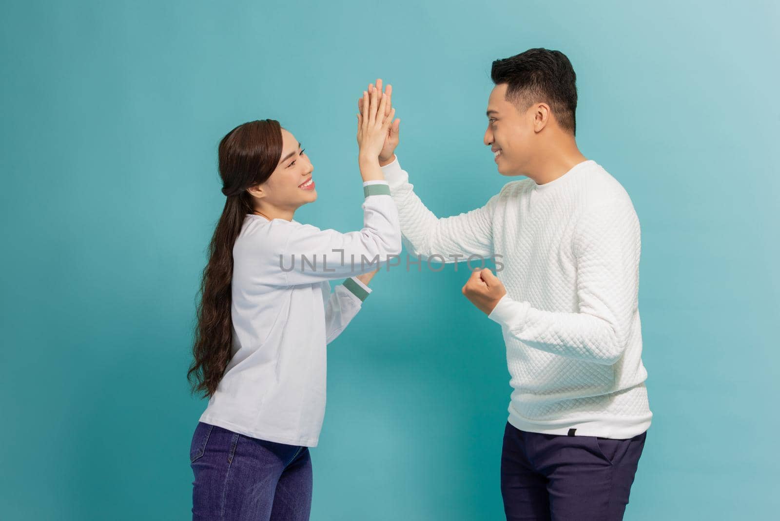 Portrait of a cheery young couple giving high five over blue background