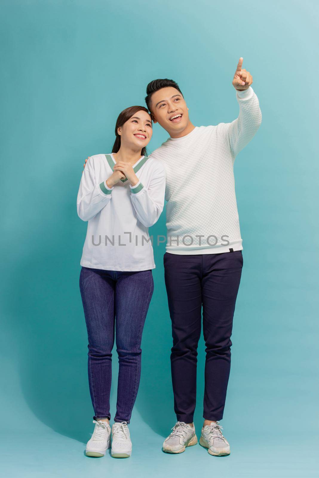 Young asian couple isolated on blue background pointing finger to the side