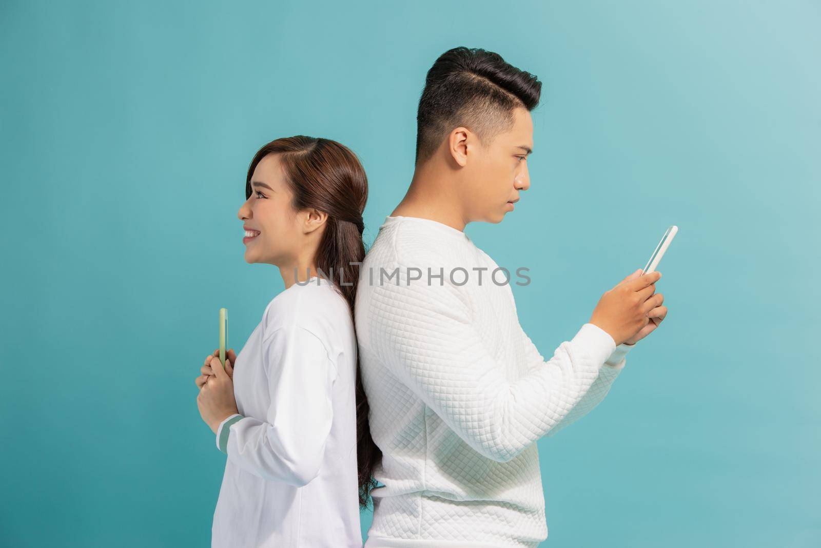 Distrust Concept. Beautiful young modern couple with smartphones in hands standing back to back.