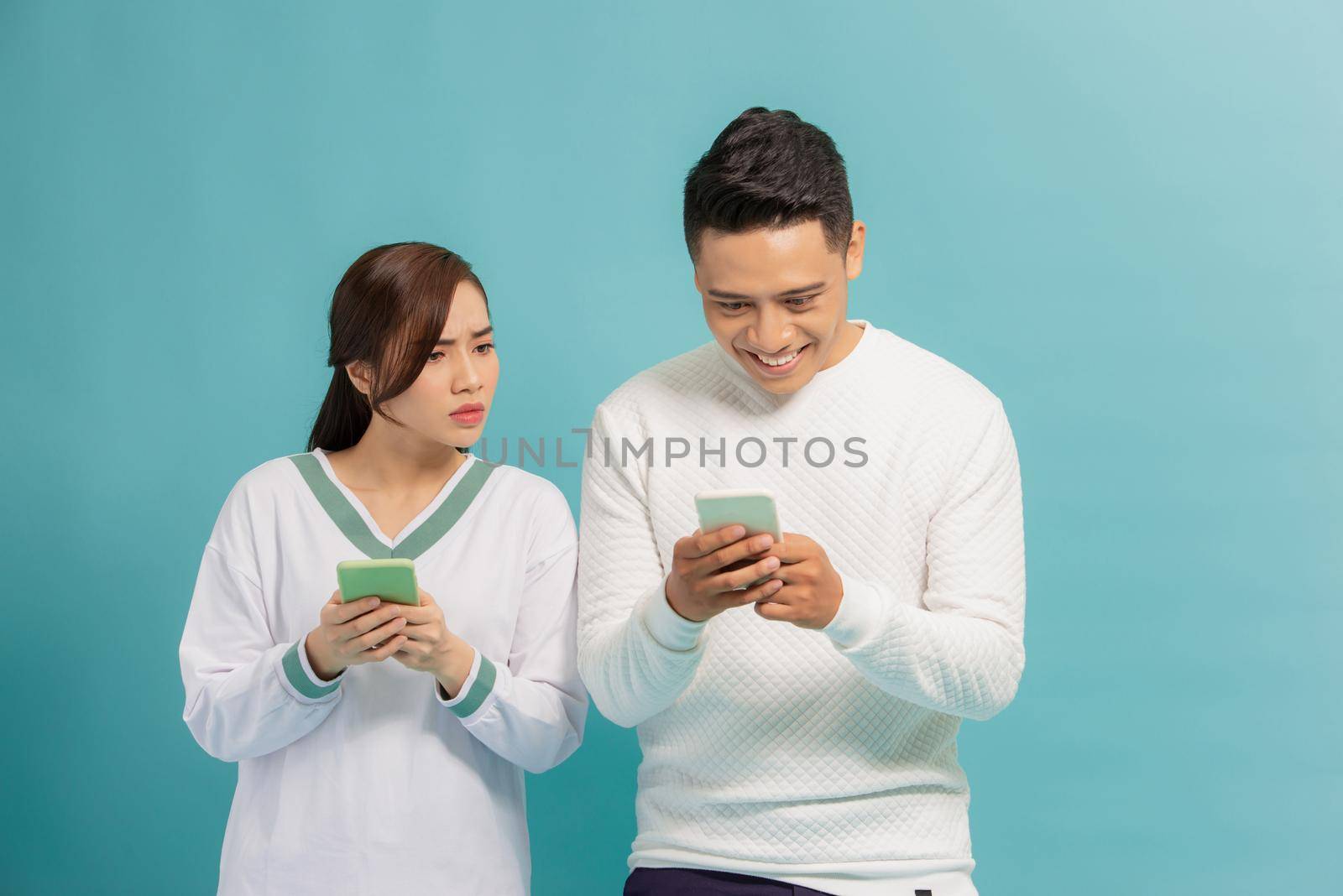 Curious woman spying and peeping at smartphone of his boyfriend while They standing together over light background by makidotvn