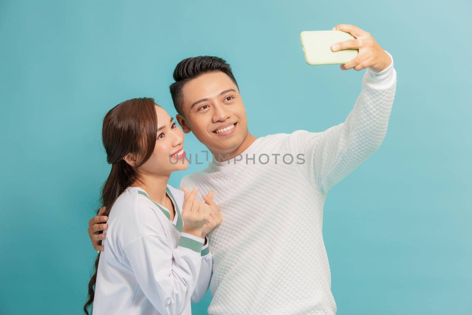 Happy young couple showing heart korean style while taking a selfie together isolated over blue background by makidotvn