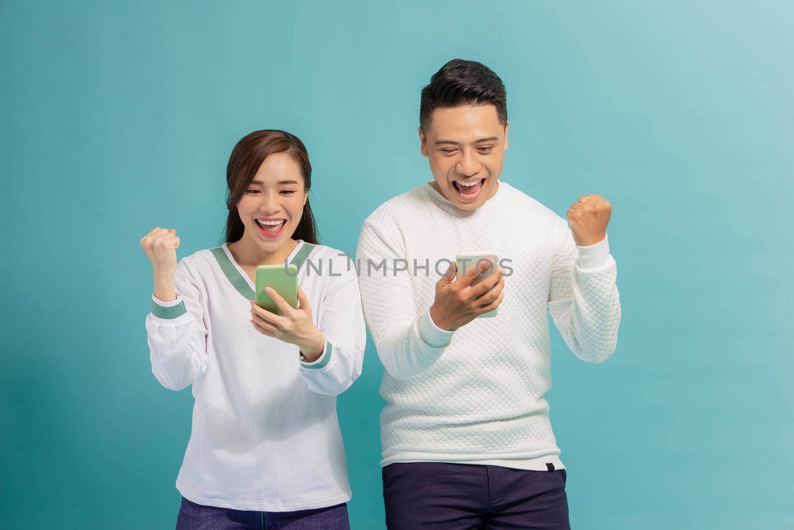 Surprised young couple stand isolated on blue background hold smartphones happy win online lottery, by makidotvn