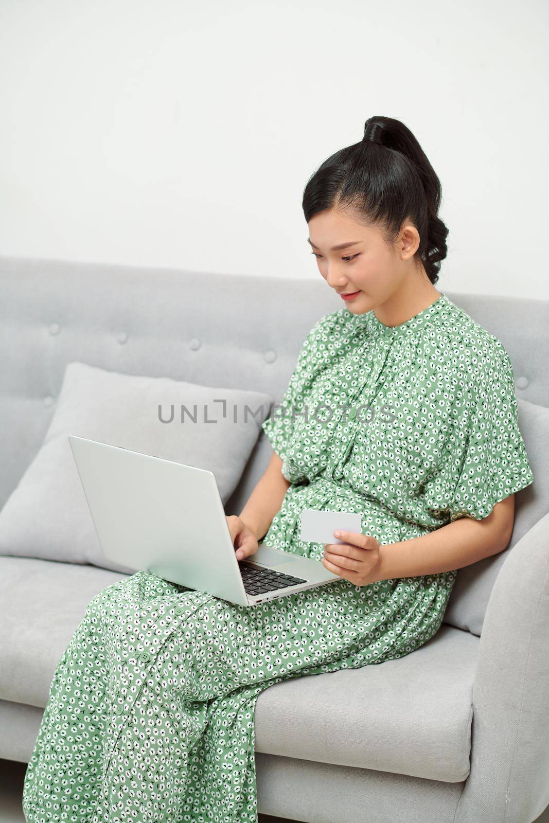 Asian pregnant mother ordering clothes for her baby, using laptop computer and credit card at home