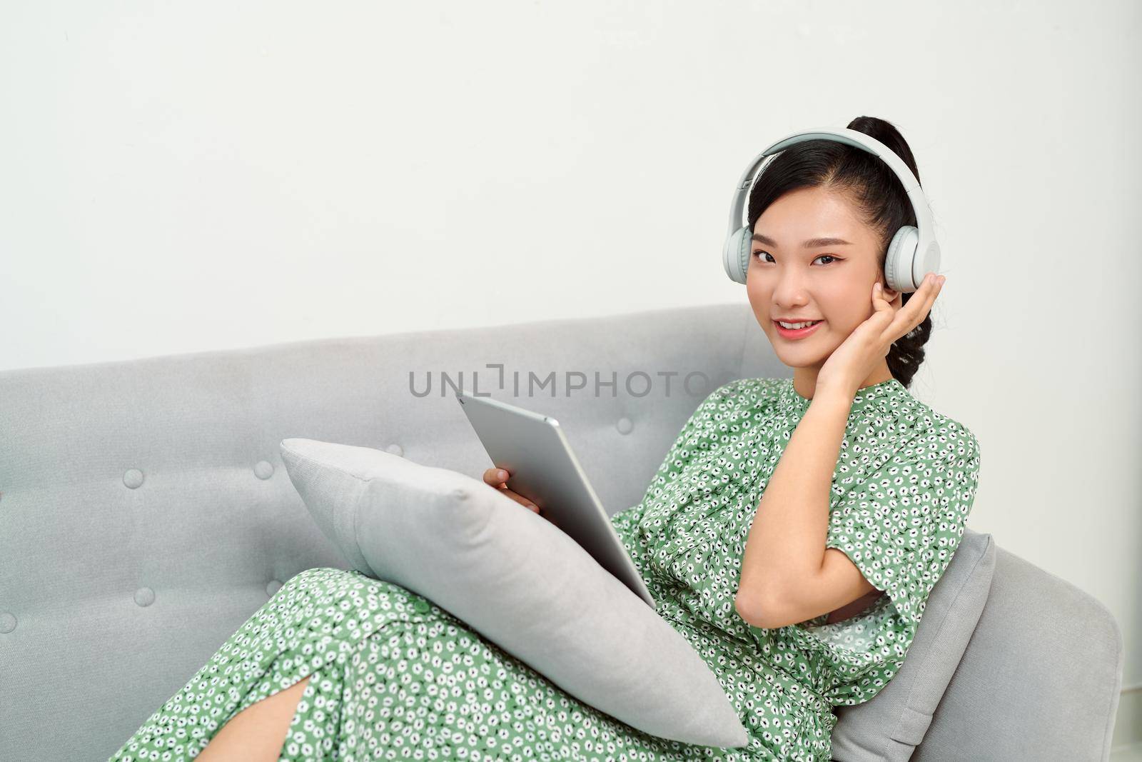 Girl listening music on line with a tablet sitting on a sofa in the living room at home