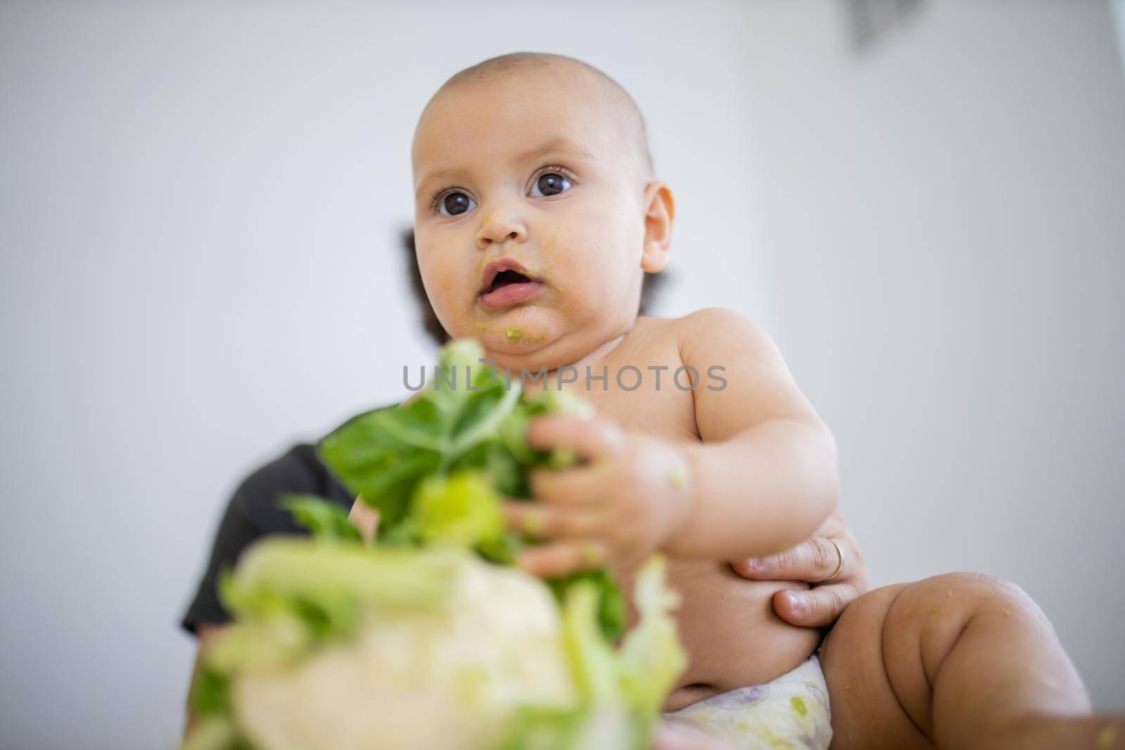 Adorable baby on a table holding a cauliflower by Kanelbulle