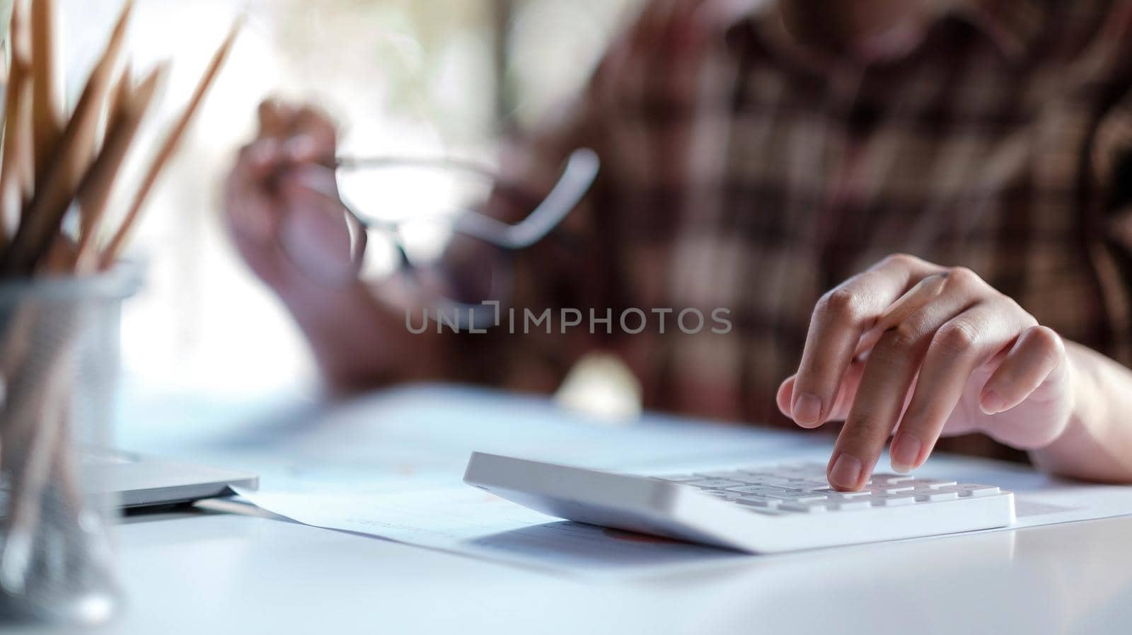 Close up of woman or accountant hand holding pen working on calculator to calculate business data, accountancy document and laptop computer at office by wichayada