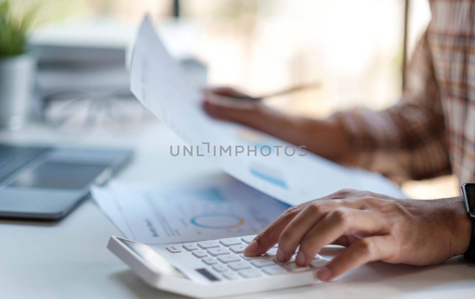 Businessman or accountant hand holding pen working on calculator to calculate business data, accountancy document with laptop computer on desks. by wichayada