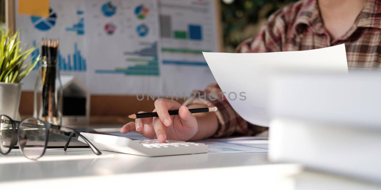 Photo of hands holding pencil and pressing calculator buttons over documents by wichayada