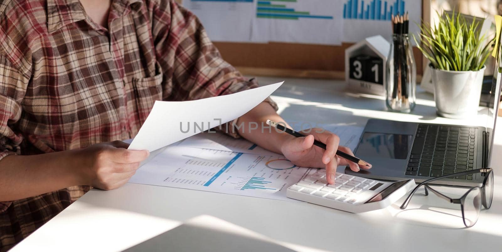 Photo of hands holding pen under document and pressing calculator buttons by wichayada