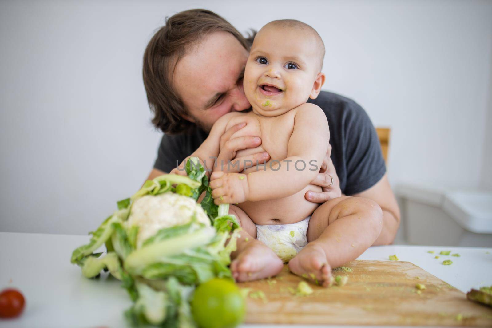 Father holding and kissing his baby daughter above a table by Kanelbulle