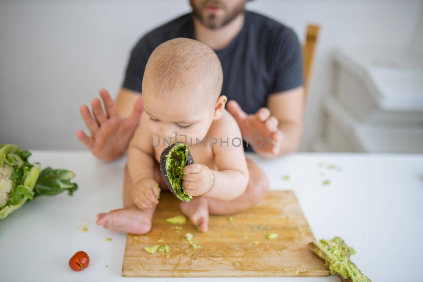 Happy baby sitting on a wooden board and biting an avocado peel by Kanelbulle