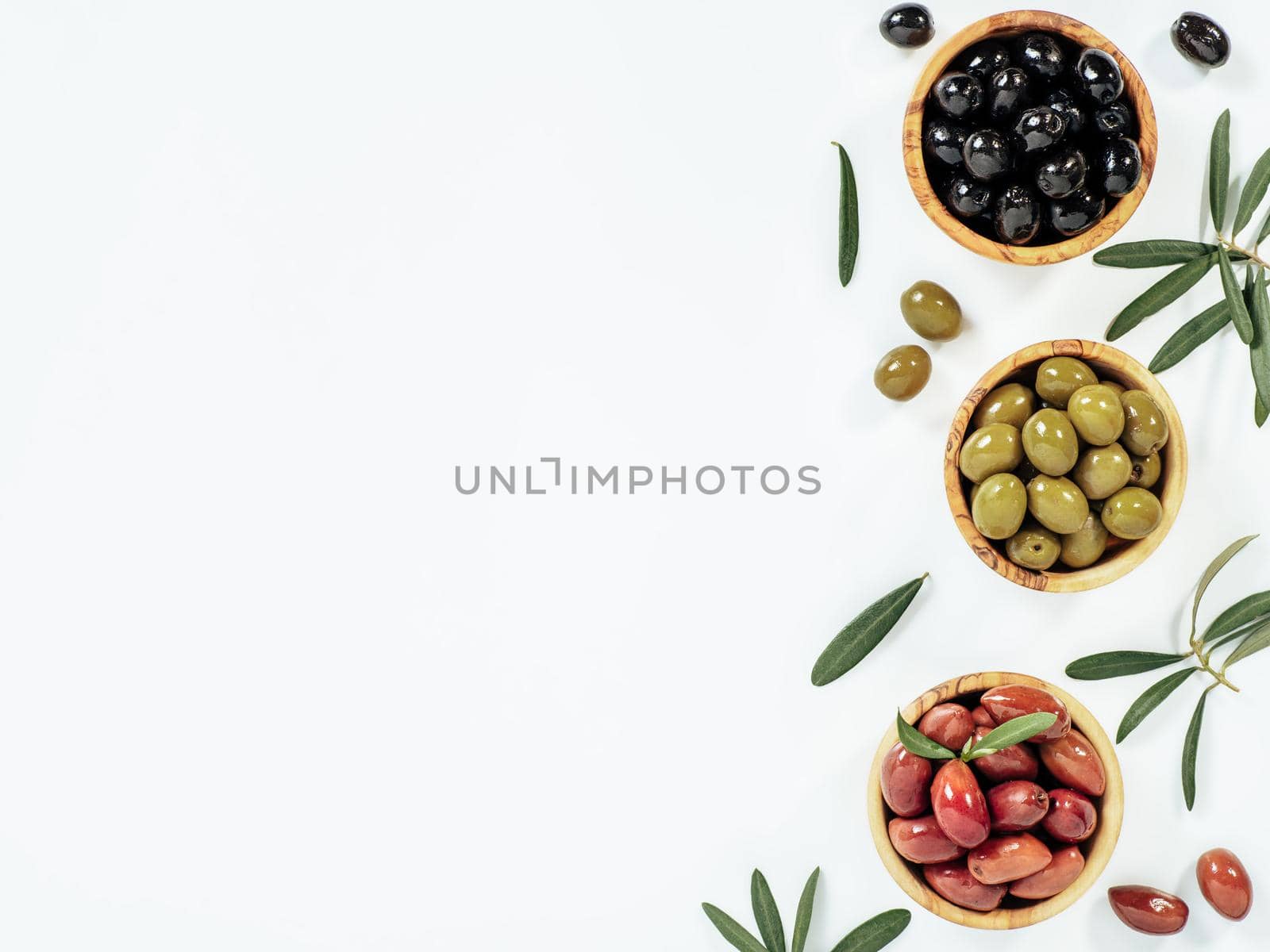 Set of green olives, black olives and red kalmata olives on white background,copy space. Top view of different olives types in bowls and leaves and branches isolated on white. Beautiful olive flat lay