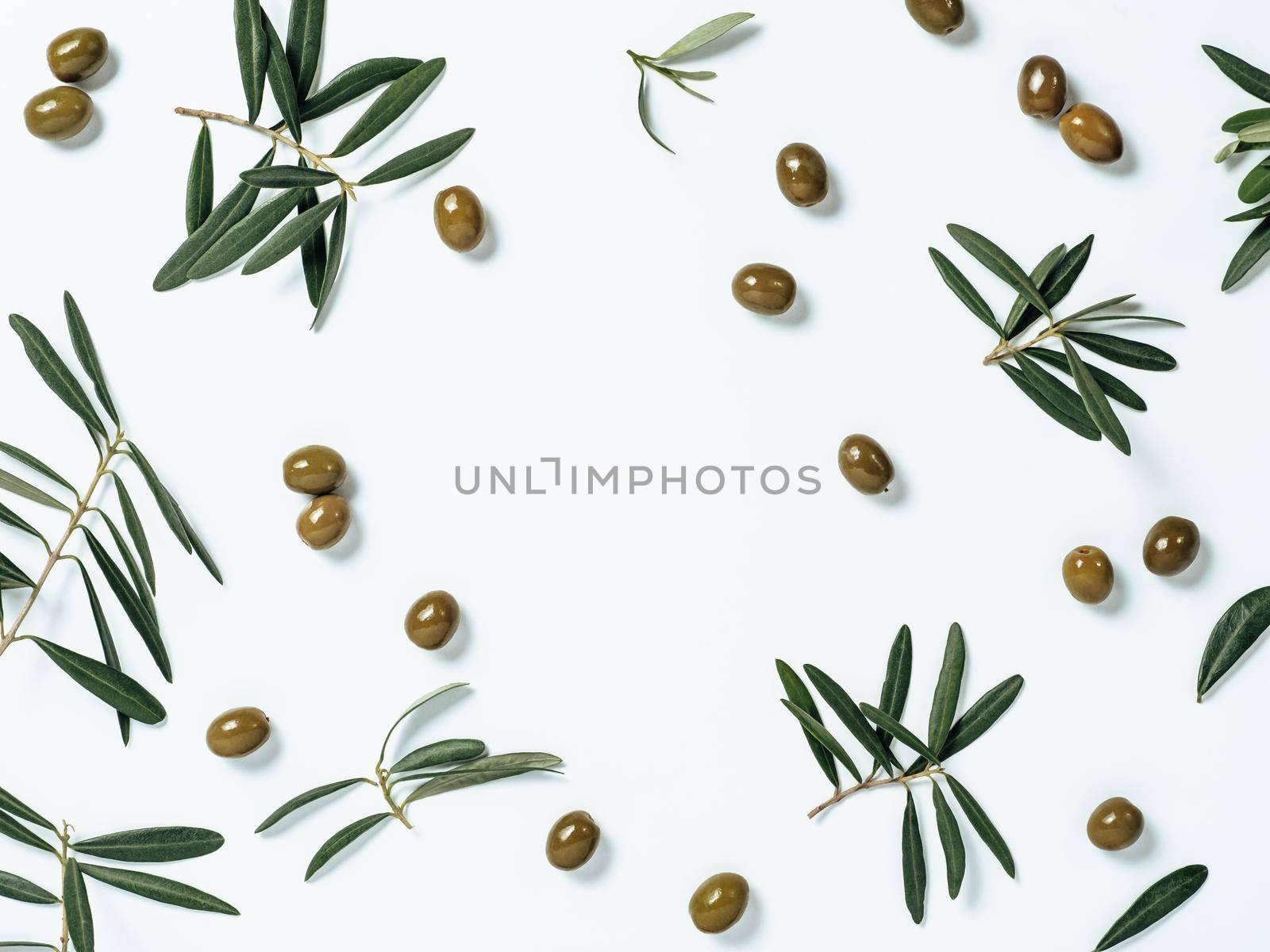Pattern with green olives and olives tree leaves and branches on white background, copy space in center. Olive tree fruits and branches, top view or flat lay.