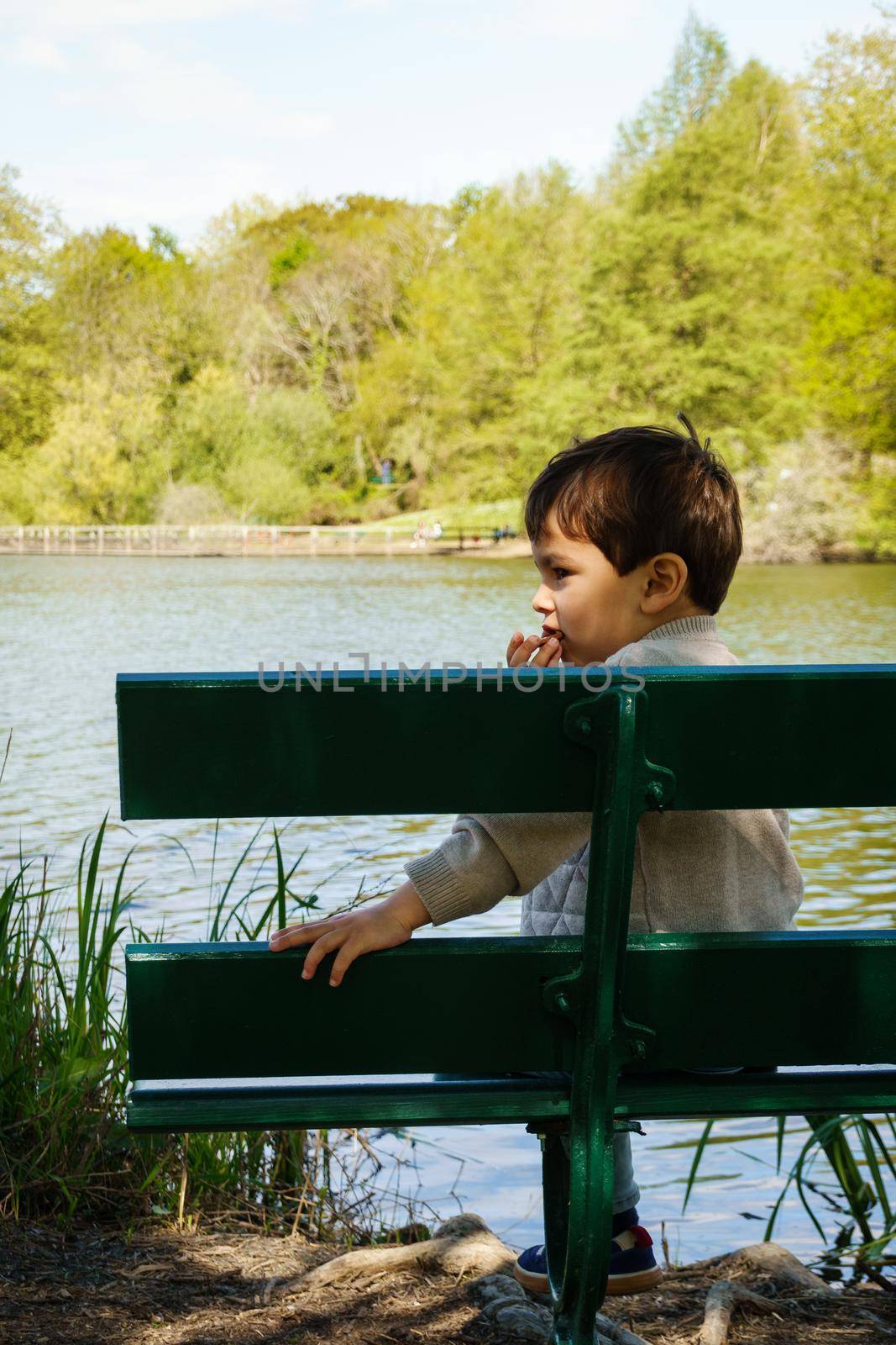 Little boy eating a biscuit on bench on lakeshore, spring season