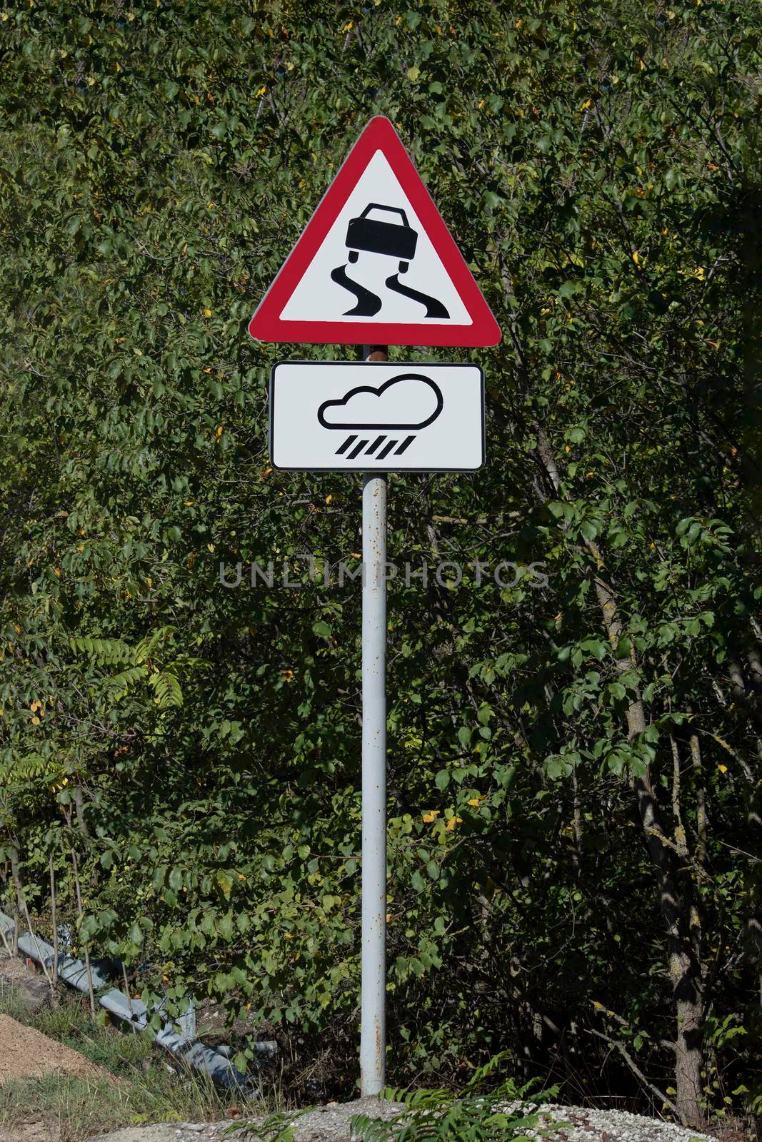 Sign road slippery road in the rain. Sunny autumn day. Front view by Essffes