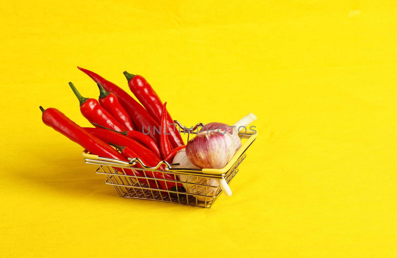 A shopping basket with vegetables and spices in the supermarket. Red pepper and fresh garlic in the shopping basket. Yellow background, with a place for inscription. High quality photo