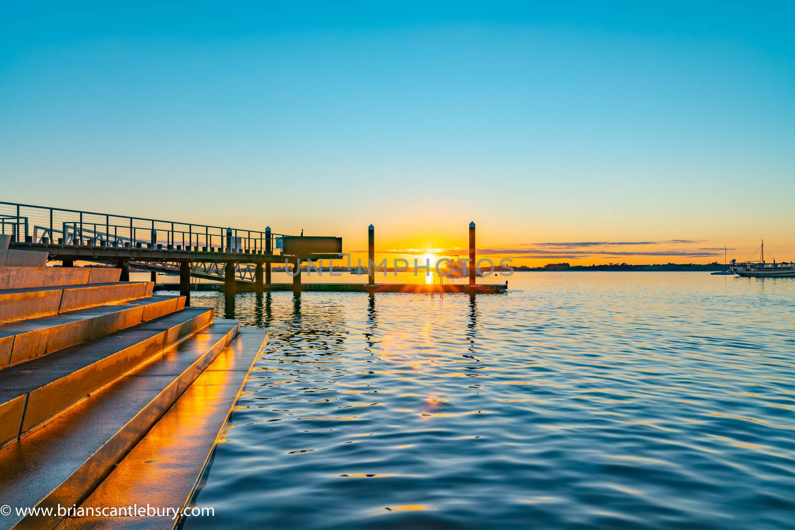 Sunrise over blue water of Tauranga harbour with intense golden glow on horizon with harbour steps and jumping platform.