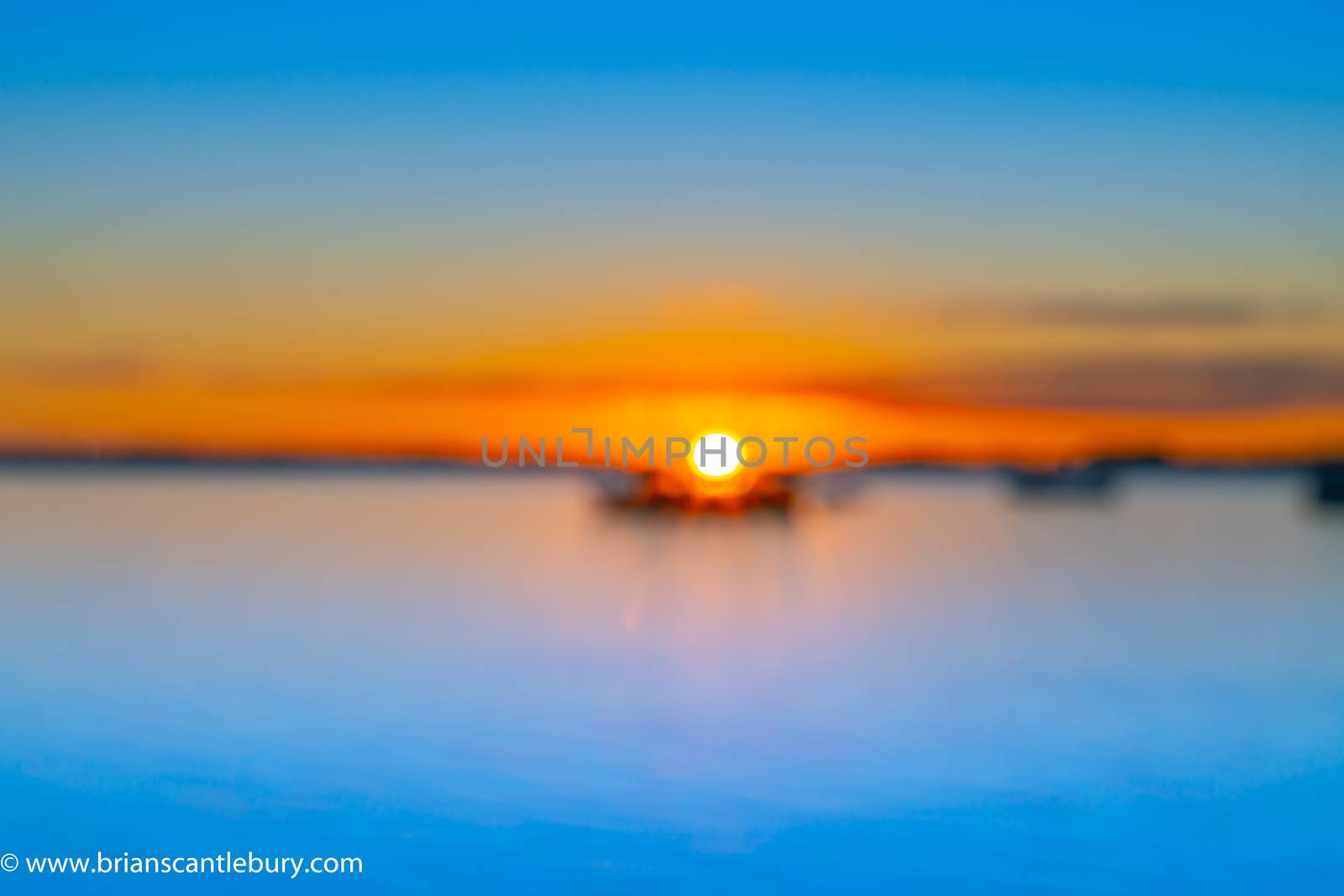 Abstract deliberate defocus coastal background for travel or coastal effects use sunrise over blue water of Tauranga harbour with intense golden glow on horizon.