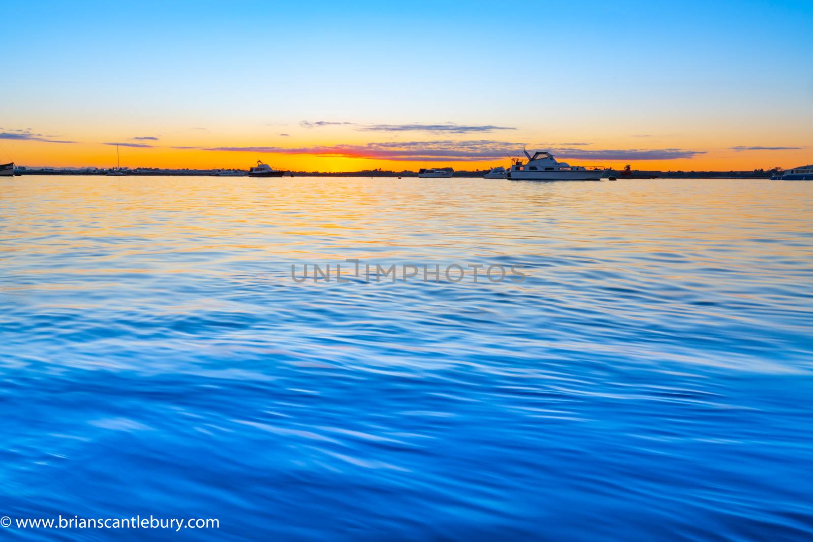 Sunrise over blue water of Tauranga harbour with intense golden glow on horizon.