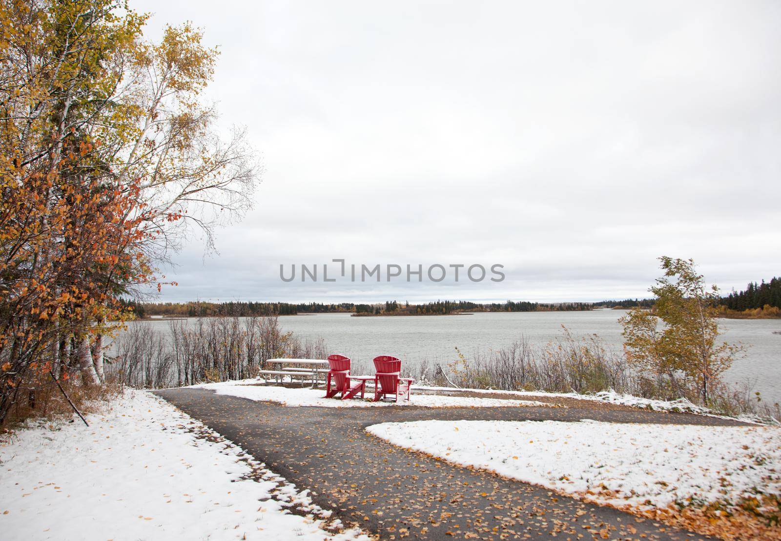 at Astotin Lake in Alberta, two red adirondack chairs celebrating Canada's 150th sit at the end of a path and overlook a lake in winter