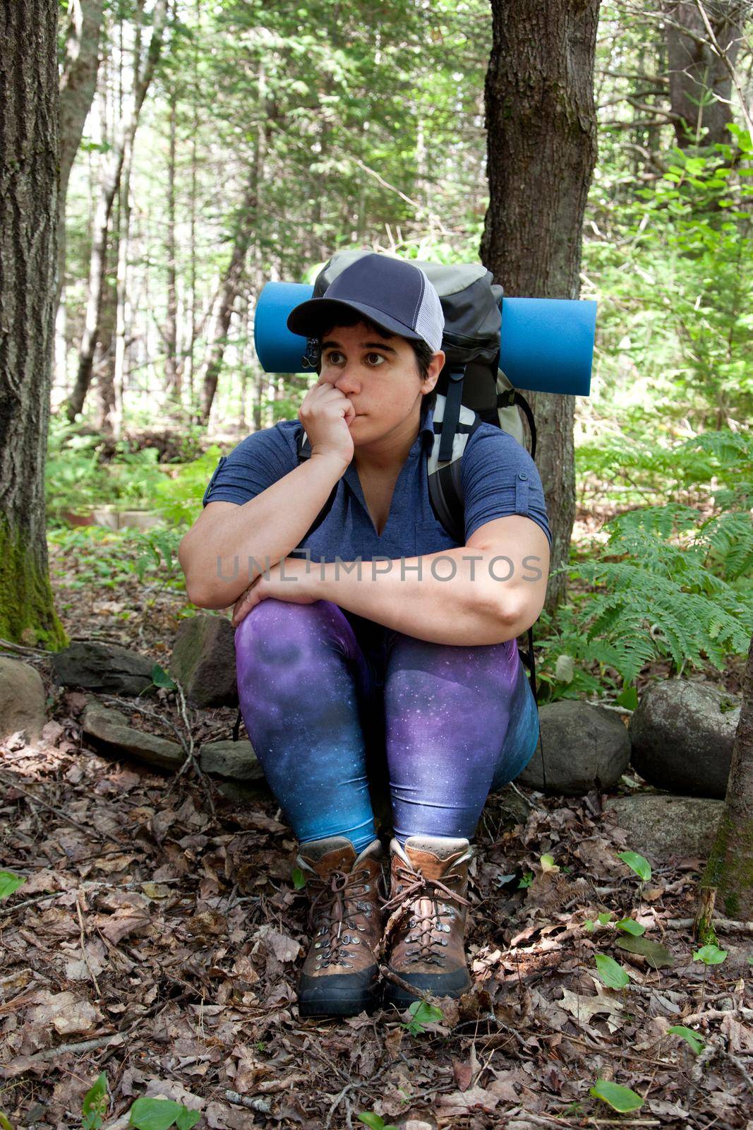 A woman sits on a rock looking puzzled or lost while hiking in the woods 